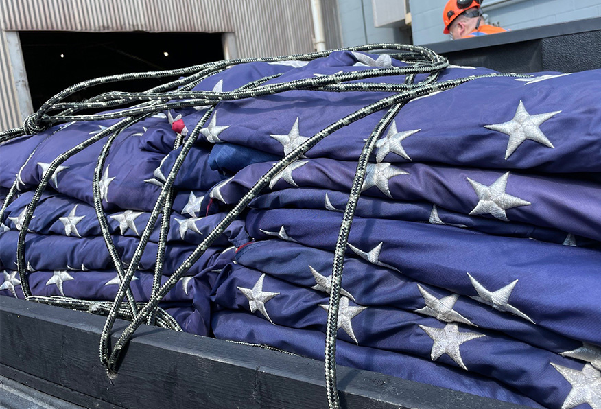A folded American flag is draped over a surface, secured with coiled ropes, displaying the stars against a blue background, suggesting a ceremonial or respectful context.