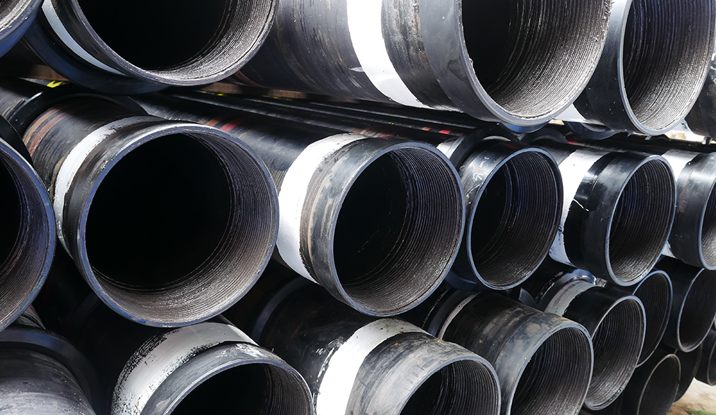 A stack of large industrial black pipes with flanged ends, likely for plumbing or construction purposes, showing concentric circles and reflective surfaces.