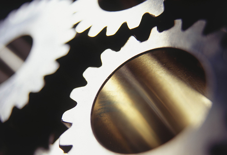 A person is working with machinery in a dimly lit setting, wearing protective glasses and focused on adjusting a component with a green light source nearby.