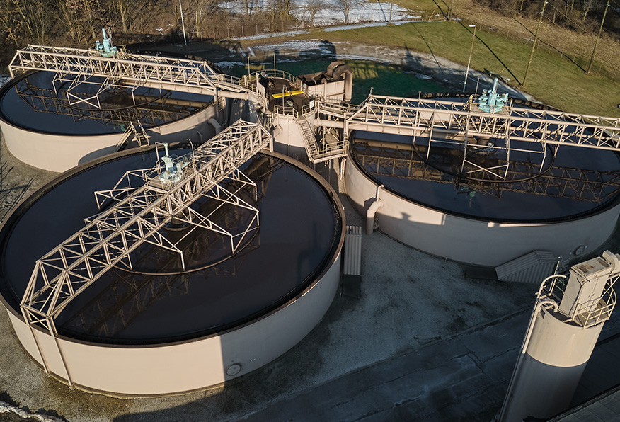 Aerial view of a water treatment plant featuring several large circular tanks with central rotating arms, surrounded by infrastructure on a clear day.