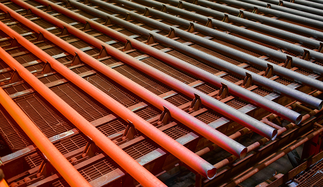 The image shows a symmetrical, angled view of red parallel metal pipes, potentially part of a large-scale industrial, manufacturing, or construction framework.